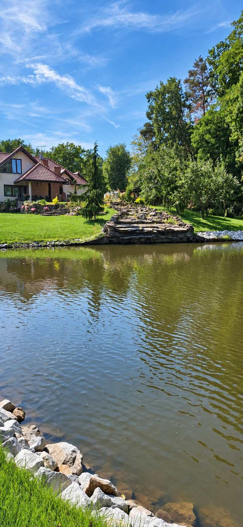 Staw z kamiennym brzegiem, w tle dom i ogród